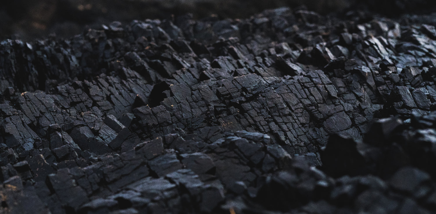Natural coal - A photo of a pile of coal in its natural form, as it is mined from the earth. The photo shows black or brownish-black coal with a rough texture and irregular shapes. Coal is a sedimentary rock that forms from the remains of plants that lived and died millions of years ago. It is a fossil fuel that is primarily composed of carbon, along with various other elements such as hydrogen, oxygen, nitrogen, and sulfur. 