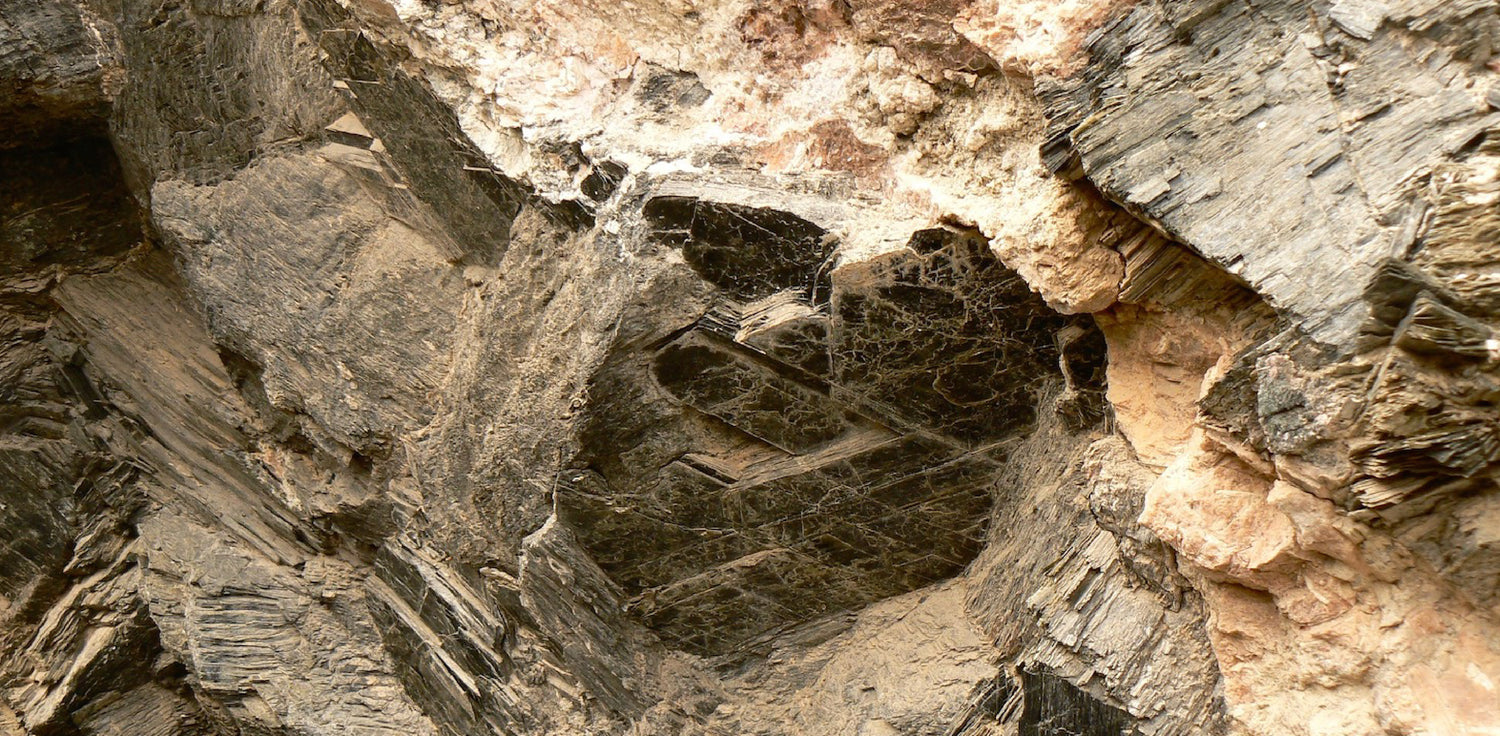 Mica deposit - A photo of a mica deposit, a group of shiny, sheet-like minerals that are often found in layered formations. The mica crystals have a characteristic platy structure and exhibit a metallic or pearlescent luster. The colors of the mica crystals can vary, including shades of silver, gold, brown, and green. 